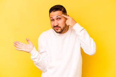 İspanyol genç adam sarı arka planda izole edilmiş ve elinde bir ürün tutuyor..