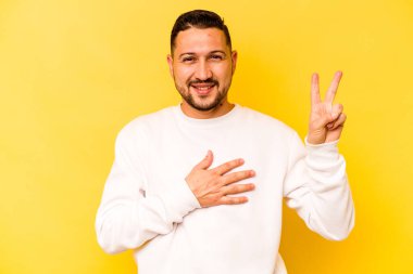 Sarı arka planda izole edilmiş genç İspanyol bir adam yemin ediyor, elini göğsüne koyuyor..