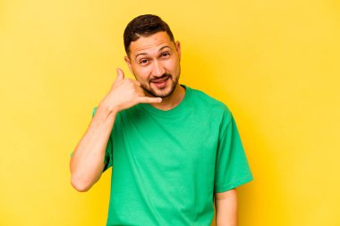 Sarı arka planda izole edilmiş genç bir İspanyol, parmakları olan bir cep telefonu hareketi gösteriyor..