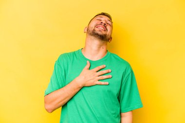 Sarı arka planda izole edilmiş genç İspanyol adam yüksek sesle gülüyor ve elini göğsüne koyuyor..