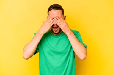 Sarı arka planda izole edilmiş genç İspanyol adam elleriyle gözlerini kapatıyor, geniş bir gülümsemeyle bir sürpriz bekliyor..