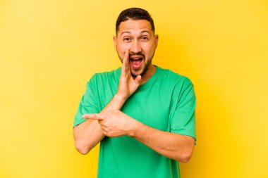 Latin kökenli genç bir adam sarı arka planda izole edilmiş. Dedikodu yapıyor, bir şeyleri bildiriyor..