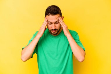 Sarı arka planda izole edilmiş genç İspanyol adam şakaklara dokunuyor ve baş ağrısı çekiyor..