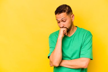 Genç İspanyol adam sarı arka planda izole edilmiş şüpheli ve şüpheci bir ifadeyle yana bakıyor..