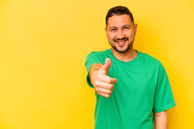Young hispanic man isolated on yellow background smiling and raising thumb up clipart