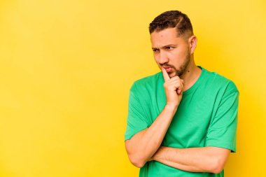 Genç İspanyol adam sarı arka planda izole edilmiş şüpheli ve şüpheci bir ifadeyle yana bakıyor..