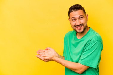 Sarı arka planda izole edilmiş genç İspanyol bir adam avucunun içinde bir kopyasını tutuyor..