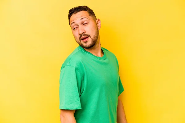 Young hispanic man isolated on yellow background looks aside smiling, cheerful and pleasant.