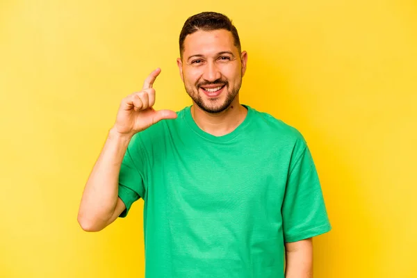 Mladý Hispánec Izolovaný Žlutém Pozadí Drží Něco Málo Ukazováčky Usmívá — Stock fotografie