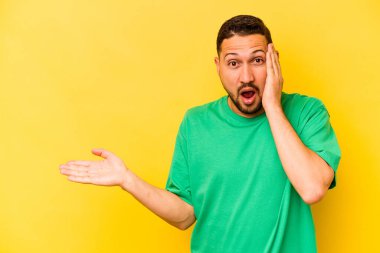 Sarı arka planda izole edilmiş genç İspanyol adam, avuç içinde kopya alanı tutmaktan etkilenmiş..