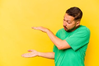 Sarı arka planda izole edilmiş genç İspanyol adam elleri arasında bir kopya alanı tutarken şok ve hayrete düştü..