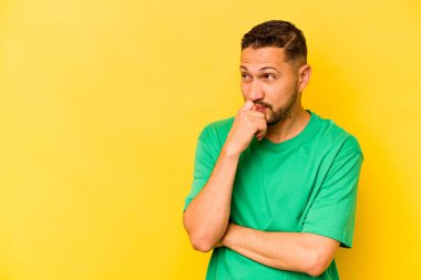 Sarı arka planda izole olmuş genç İspanyol bir adam rahatlamış bir şeyin fotokopi odasına baktığını düşünüyor..