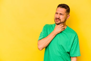 Genç İspanyol bir adam sarı arka planda izole edilmiş kafasının arkasına dokunuyor, düşünüyor ve bir seçim yapıyor..