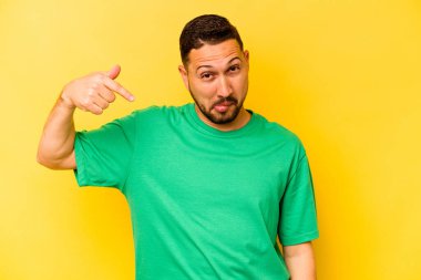 İspanyol asıllı genç adam sarı arka planda tek başına gömlek fotokopi alanını gösteriyor, gururlu ve kendinden emin.