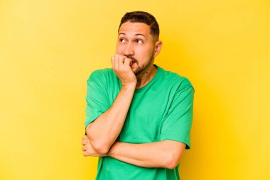 Sarı arka planda izole edilmiş, tırnak yiyen, gergin ve endişeli genç bir adam..