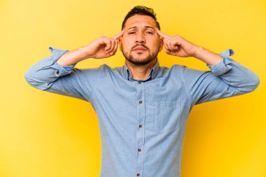 Sarı arka planda izole edilmiş genç İspanyol adam bir göreve odaklanmış, işaret parmaklarını işaret ediyor..