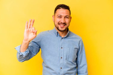 Genç İspanyol adam sarı arka planda izole edilmiş neşeli ve kendinden emin..