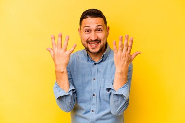 Sarı arka planda izole edilmiş genç İspanyol adam on numarayı elleriyle gösteriyor..