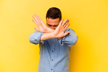 Sarı arka planda izole edilmiş genç İspanyol adam iki kolu çapraz tutuyor, inkar kavramı.