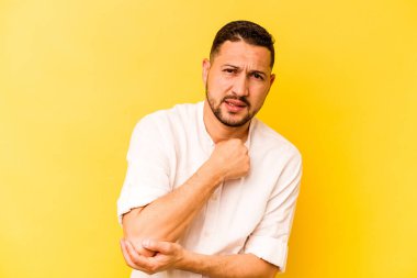 Genç İspanyol adam sarı arka planda izole edilmiş dirsek masajı yapıyor, kötü bir hareketin ardından acı çekiyor..