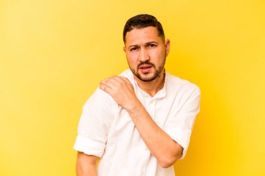 Sarı arka planda izole edilmiş, omuz ağrısı olan genç bir İspanyol..