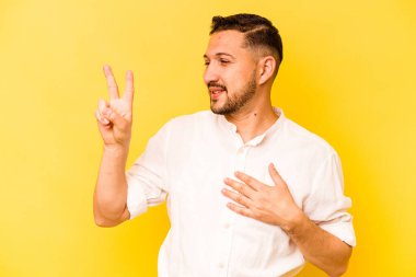 Sarı arka planda izole edilmiş genç İspanyol bir adam yemin ediyor, elini göğsüne koyuyor..