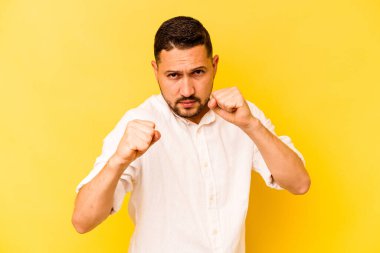 Latin kökenli genç bir adam sarı arka planda izole edilmiş. Yumruk atıyor, sinirleniyor, kavga ediyor..