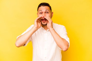 Latin kökenli genç bir adam sarı arka planda izole edilmiş. Dedikodu yapıyor, bir şeyleri bildiriyor..