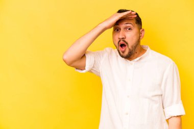 Genç İspanyol adam sarı arka planda izole edilmiş, uzaklara bakıyor ve elini alnına koyuyor..