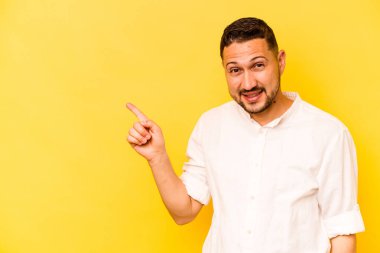 Sarı arka planda izole edilmiş genç İspanyol adam işaret parmağıyla işaret ederek gülümsüyor..