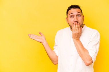 Sarı arka planda izole edilmiş genç İspanyol adam, avuç içinde kopya alanı tutmaktan etkilenmiş..
