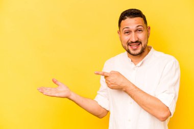 Sarı arka planda izole edilmiş genç İspanyol bir adam heyecanlı bir şekilde avuç içinde bir kopyasını tutuyor..