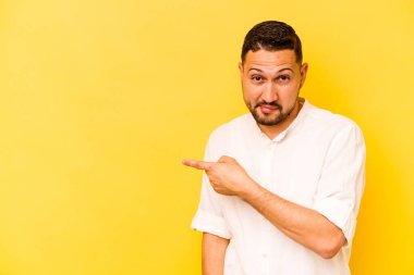 Sarı arka planda izole edilmiş genç İspanyol adam gülümsüyor ve boş alanda bir şeyler gösteriyor..