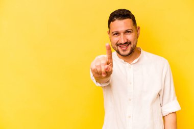 Sarı arka planda izole edilmiş genç İspanyol bir numara parmağıyla görünüyor..