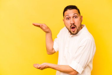 Sarı arka planda izole edilmiş genç İspanyol adam elleri arasında bir kopya alanı tutarken şok ve hayrete düştü..