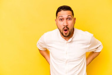 Genç İspanyol adam sarı arka planda izole edilmiş. Gördüğü bir şey yüzünden şoka uğruyor..