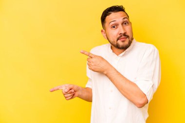 Sarı arka planda izole edilmiş genç İspanyol adam işaret parmağıyla fotokopi alanını işaret ederek şok oldu..