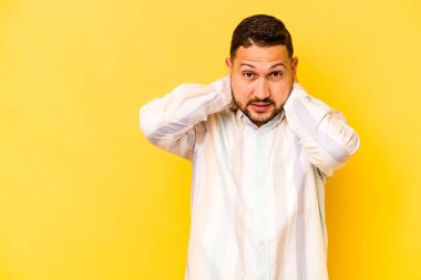 Genç İspanyol bir adam sarı arka planda izole edilmiş kafasının arkasına dokunuyor, düşünüyor ve bir seçim yapıyor..