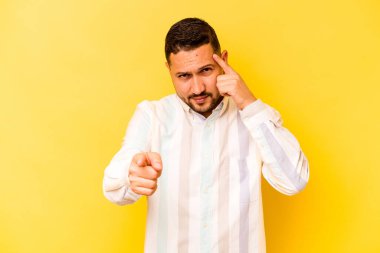 Sarı arka planda izole edilmiş genç İspanyol bir adam şakağı parmağıyla işaret ediyor, düşünüyor ve bir göreve odaklanıyor..