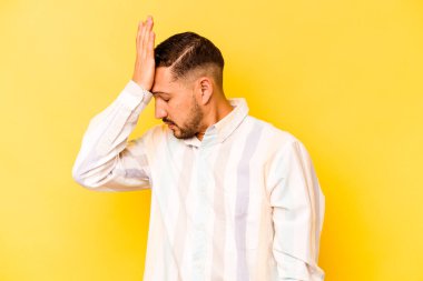 Sarı arka planda izole edilmiş genç bir İspanyol bir şeyi unutuyor. Alnına avuç içi ve gözlerini kapatıyor..