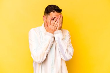 Sarı arka planda izole edilmiş genç bir İspanyol parmaklarıyla gözünü kırp korkmuş ve gergin..