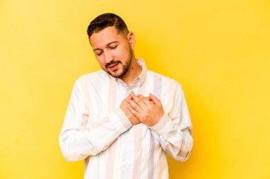 Sarı arka planda izole edilmiş genç İspanyol bir adam dost canlısı bir ifadeye sahip, avuçlarını göğsüne bastırıyor. Aşk konsepti.