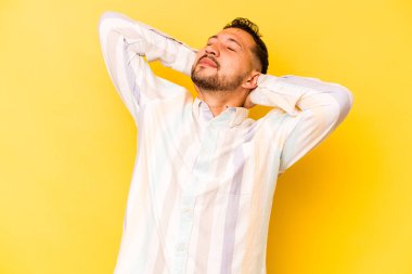 İspanyol genç adam sarı arka planda izole edilmiş. Kendine güveniyor, elleri başının arkasında..