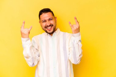 Sarı arka planda izole edilmiş genç İspanyol bir adam boynuzlarını devrim konsepti olarak gösteriyor..