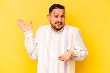 Sarı arka planda izole edilmiş genç İspanyol bir adam. Kafası karışmış ve omuz silkiyor. Kopya alanını tutmak için..