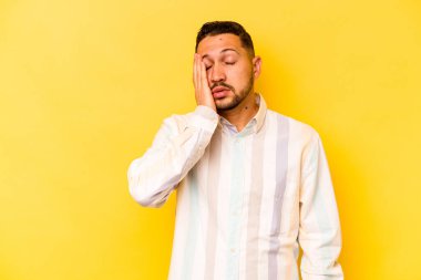 Sarı arka planda izole edilmiş genç bir İspanyol. Çok yorgun ve uykulu. Elini başının üstünde tutuyor..