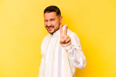 Sarı arka planda izole edilmiş genç İspanyol adam iki numarayı parmaklarıyla gösteriyor..