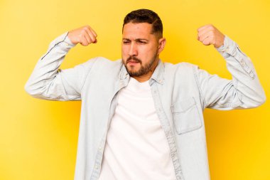 Sarı arka planda izole edilmiş genç bir İspanyol kadın gücünün sembolü olan kollarıyla güçlü bir hareket gösteriyor.