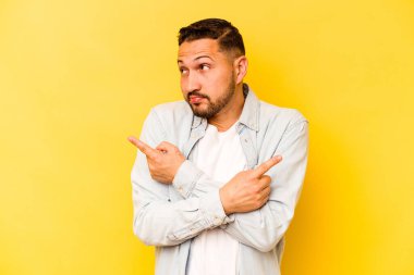 Sarı arka plan noktalarında izole edilmiş genç İspanyol adam iki seçenek arasında seçim yapmaya çalışıyor..