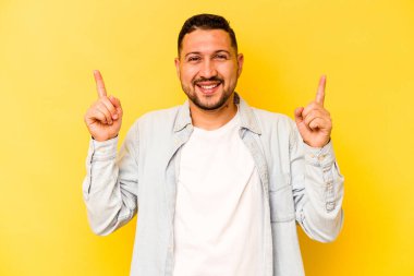 Sarı arka planda izole edilmiş genç İspanyol bir adam iki ön parmağı da boş bir alan gösteriyor..